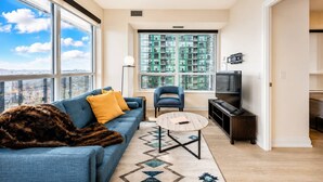 A modern living room with a sofa, armchair, coffee table, and a TV. - Cozy 2BR 2BA Condo | Steps to Subway | Pool & Gym (Toronto)
