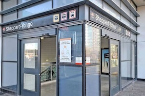 Une entrée de la station de métro Sheppard-Yonge dotée de portes en verre, d’un panneau indiquant les mesures de précaution à prendre en raison de la COVID-19 et d’un escalier bien visible menant à un escalier mécanique.