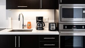 A modern kitchen with dark wood cabinets, a stainless steel sink, a coffee maker, a toaster, and a microwave.