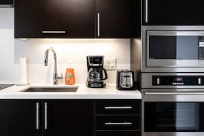 A modern kitchen with dark wood cabinets, a stainless steel sink, a coffee maker, a toaster, and a microwave.
