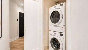 A laundry room with two stacked washing machines, a door leading to another room, and a light fixture above the machines. - Cozy 2BR 2BA Condo | Steps to Subway | Pool & Gym (Toronto)