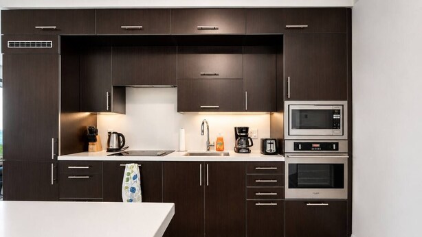A modern kitchen with dark cabinetry, stainless steel appliances, and a white countertop. - Cozy 2BR 2BA Condo | Steps to Subway | Pool & Gym (Toronto)