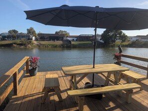 A wooden deck with a table and benches overlooking a body of water, with a large umbrella providing shade. - Tampa Area,Heated Pool, water views,3 bedroom Tampa Bay area (Port Richey)