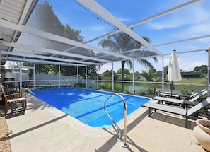 An outdoor swimming pool with a covered area, lounge chairs, and a view of a lake.