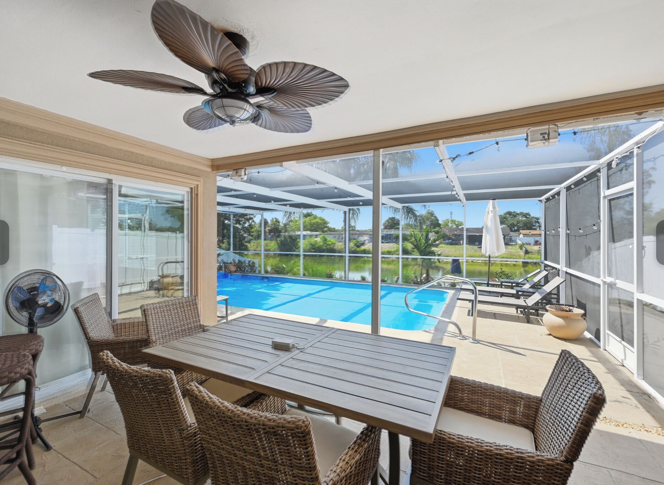 Eine sonnendurchflutete Terrasse mit Pool, Korbmöbeln und Deckenventilator.