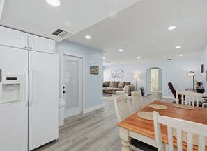 A modern kitchen with white appliances, a dining area with a wooden table and chairs, and a living room with a sofa and decorative items. - Tampa Area,Heated Pool, water views,3 bedroom Tampa Bay area (Port Richey)