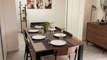 Uma área de refeições com uma mesa de madeira comprida posta para quatro pessoas, com cadeiras ao redor e uma luminária moderna em um aparador.