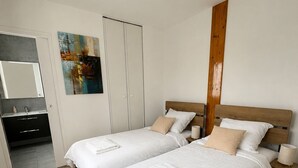 Een slaapkamer met twee bedden, een houten hoofdbord, een schilderij, een kledingkast en een badkamer met spiegel en wastafel.