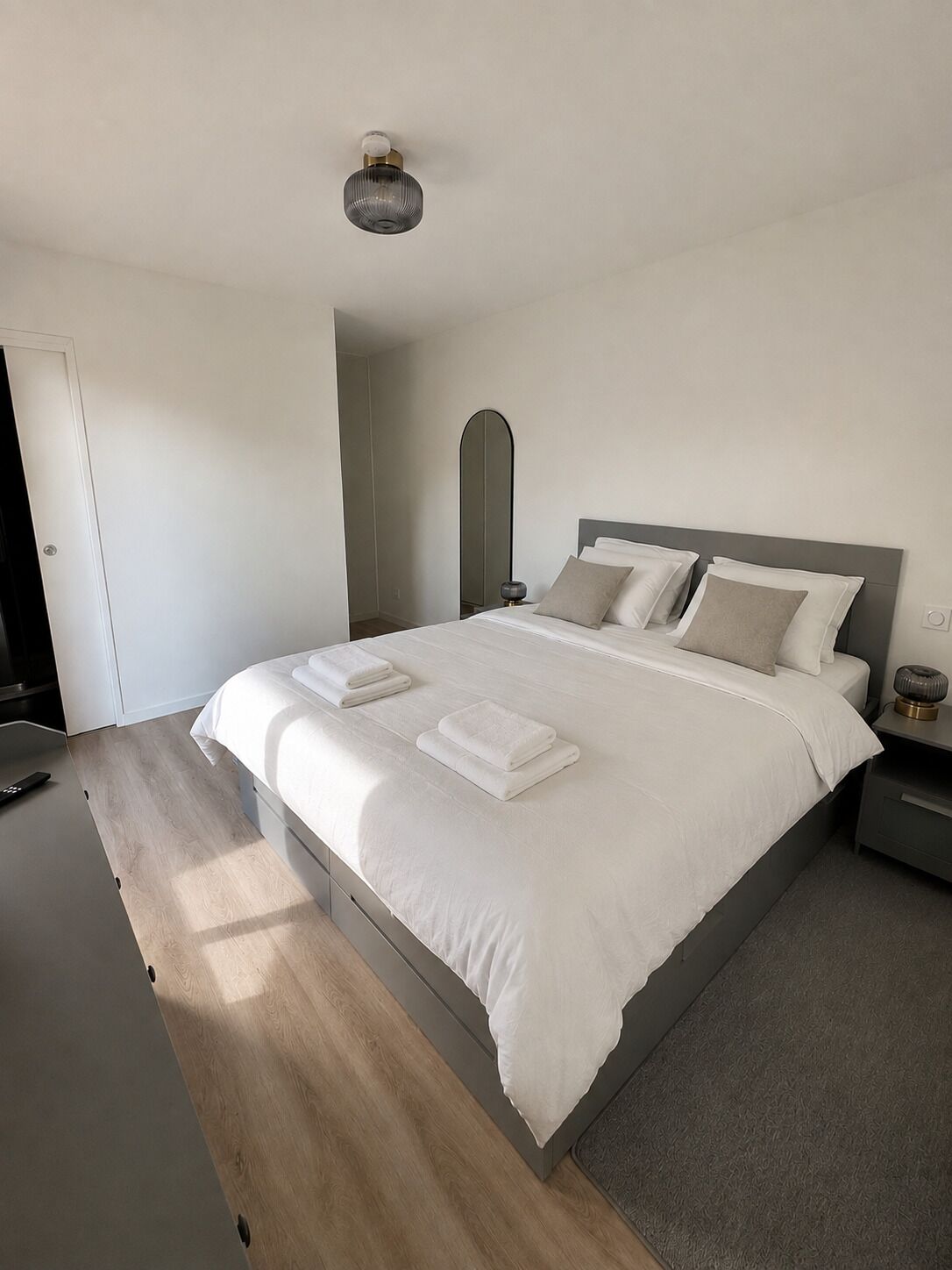 Une chambre à coucher moderne avec un grand lit, une table de chevet, une commode et un luminaire fixé au mur.
