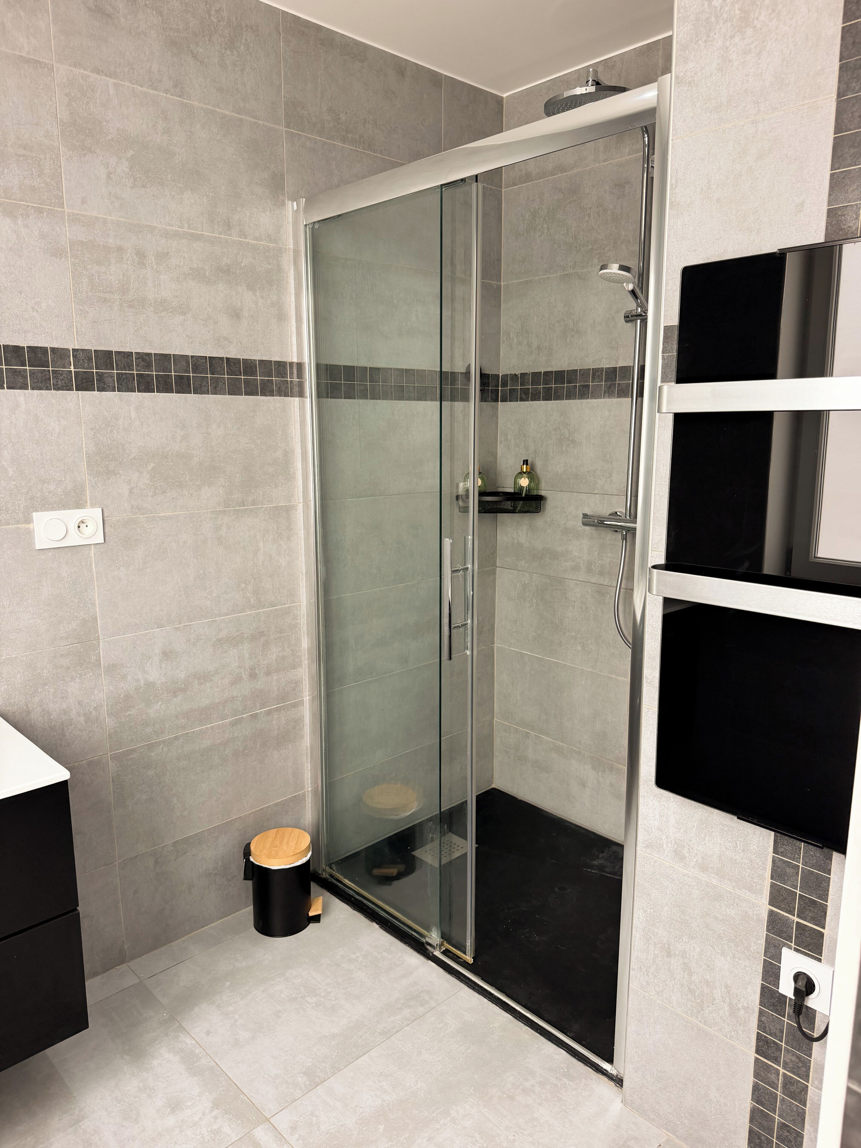 A modern bathroom with a glass-enclosed shower, a black toilet, and a black sink.