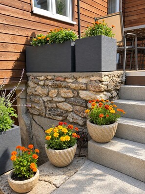 A stone wall with a wooden building in the background, outdoor steps, and potted plants with flowers. - Premium chalet 15 minutes from Disneyland and 5 minutes from Parrot World (Crécy-la-Chapelle)