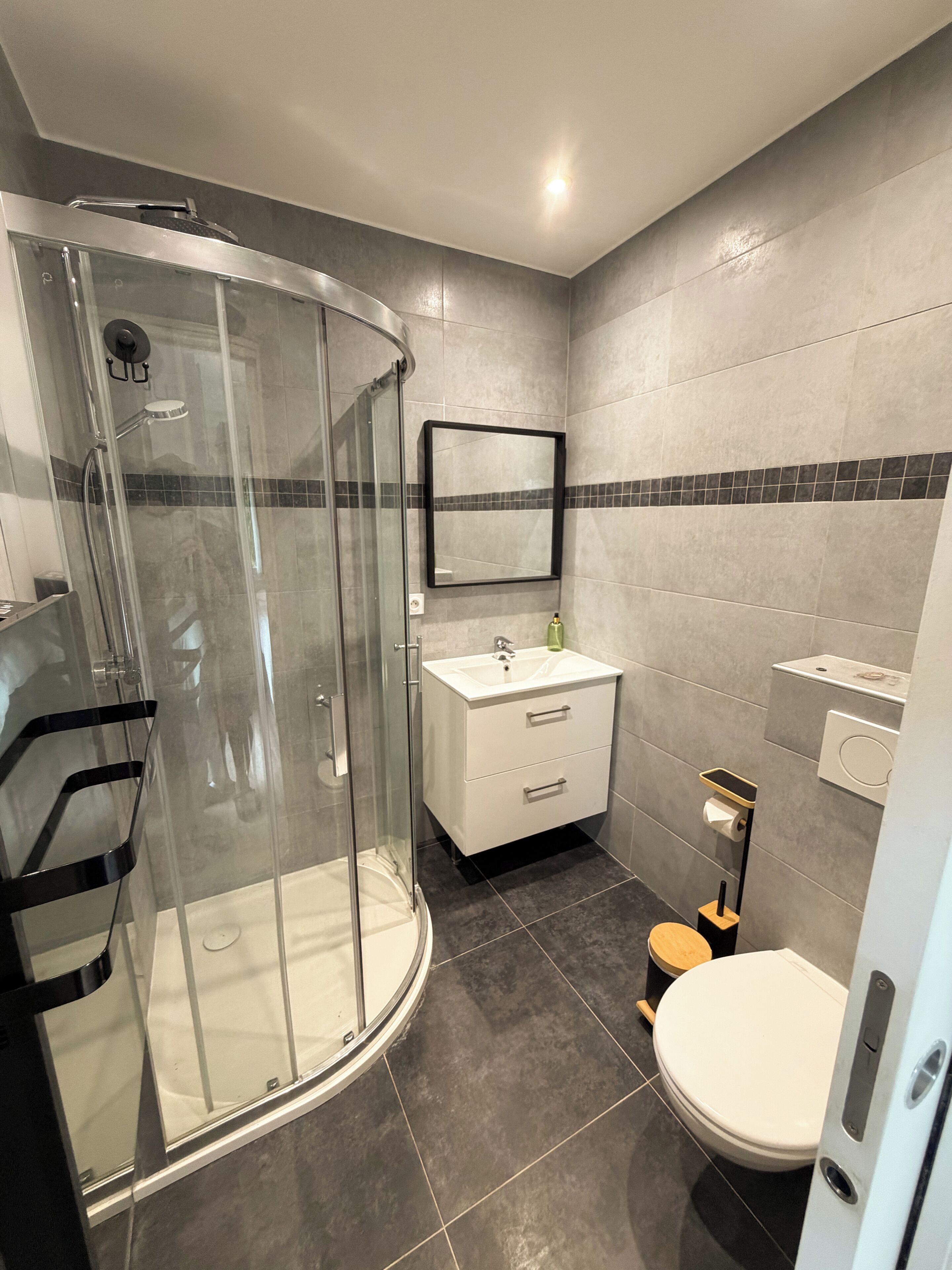 Een moderne badkamer met een douchecabine van glas, een wit wastafelmeubel en een toilet.