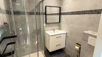 Een moderne badkamer met een douchecabine van glas, een wit wastafelmeubel en een toilet.