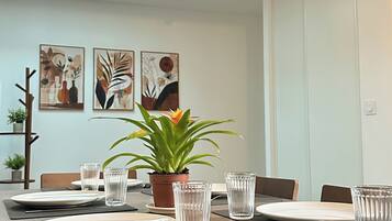 Un coin repas avec une longue table dressée pour quatre personnes, agrémentée de beaux verres, d’assiettes et de couverts. Deux plantes en pot sont posées sur la table, et la pièce présente un design moderne avec des œuvres d’art abstraites accrochées aux murs.