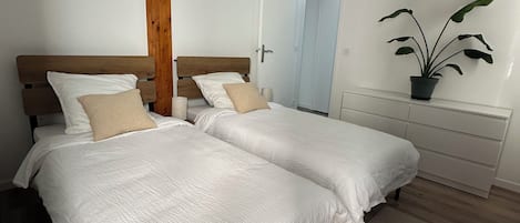 A bedroom with two beds, a wooden accent wall, a potted plant, and a white dresser.