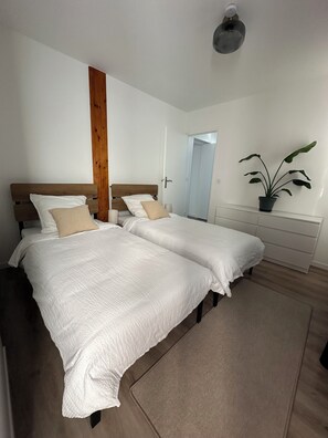 Un dormitorio con dos camas, un cabecero de madera, una planta en maceta y un aparador blanco.