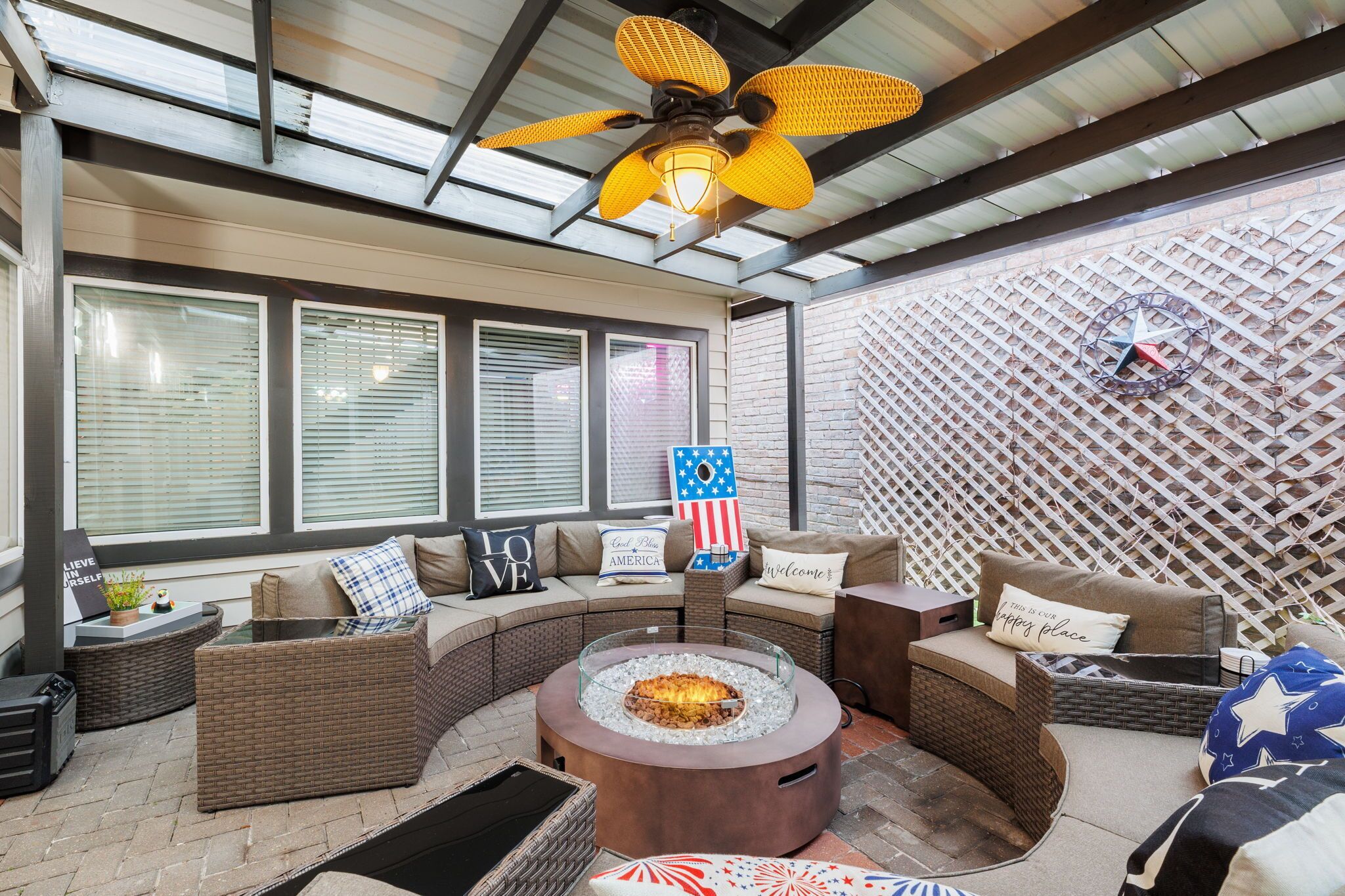 A covered outdoor seating area with a fire pit, wicker furniture, and a decorative American flag sign.