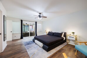 Ein Schlafzimmer mit Bett, Schreibtisch, Stuhl, Deckenventilator und Blick durch eine Glastür.