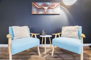 Ein Zimmer mit zwei blauen Sesseln, einem kleinen runden Tisch und einem Wandbild eines Stiers.