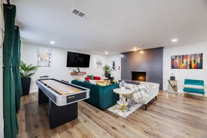 Ein modernes Wohnzimmer mit Billardtisch, grünem Sofa und Kamin.