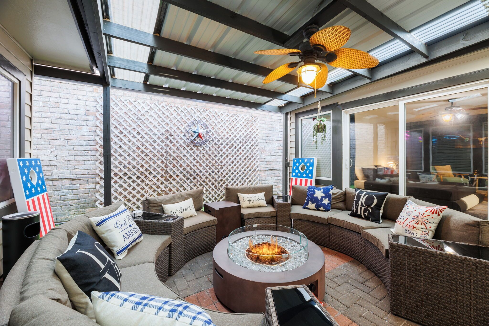 A covered outdoor seating area with a fire pit, wicker furniture, and American flag decorations.