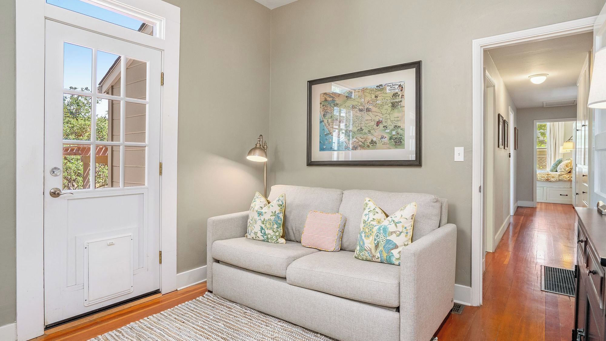 A living room with a grey sofa, a framed map on the wall, and a door with a window.