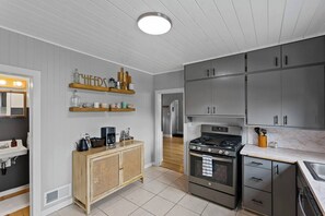 Une cuisine moderne avec des meubles gris, un meuble en bois doté de portes en osier, une cuisinière en acier inoxydable et un plan de travail en marbre.