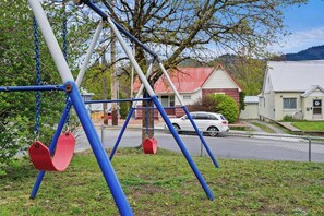 A swing set in a grassy area with houses in the background. - Rocky Mt Retreat | 2 King Beds | Bike Storage (Kellogg)