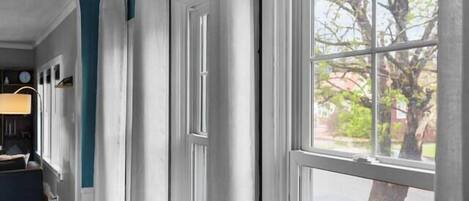 Una habitación con un gran ventanal, cortinas blancas y suelo de madera.