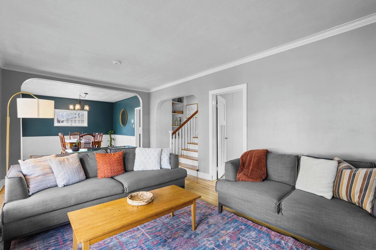 Ein Wohnzimmer mit zwei grauen Sofas, einem Holztisch und einem farbenfrohen Teppich.