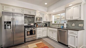 A modern kitchen with stainless steel appliances, white cabinetry, and a tiled backsplash. - Chateau Paso by Avantstay Pool Table + Private Deck Walk to Downtown Paso (Paso Robles)
