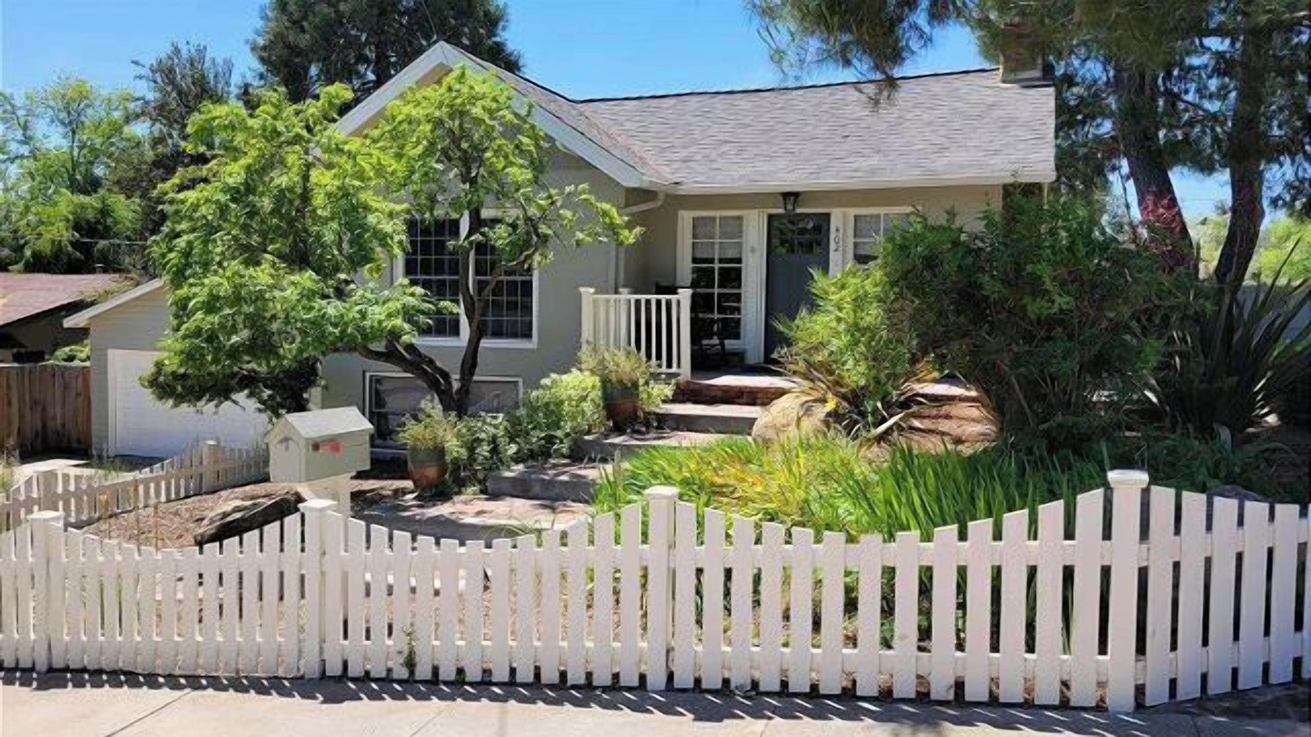 A single-story house with a white picket fence, a front porch, and a well-maintained garden.