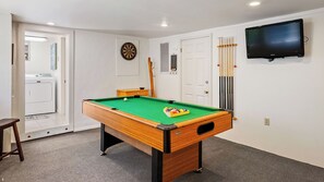 Ein Billardtisch mit Queuehalterung, eine Dartscheibe und ein Fernseher an der Wand.