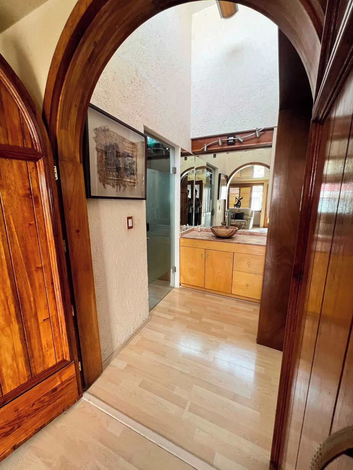 Un pasillo que lleva a una cocina con armarios de madera y un espejo grande.