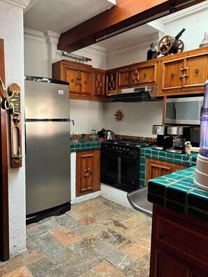 Una cocina con armarios de madera, un refrigerador de acero inoxidable, una estufa negra y un salpicadero de azulejos.