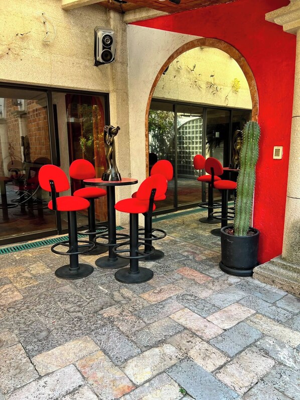 An outdoor seating area with red chairs and tables, a cactus plant, and a statue.
