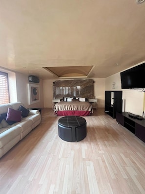 Una sala moderna con un sofá, un reposapiés y una cama grande con una colcha roja.