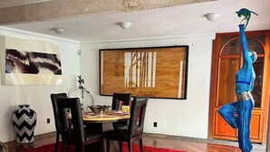 Uma sala de jantar com uma mesa de madeira, cadeiras pretas, um tapete vermelho e uma escultura azul.
