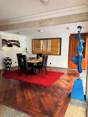 Comedor con mesa de madera, sillas negras, alfombra roja y una escultura azul.