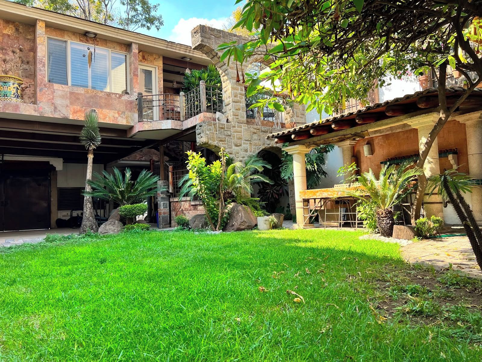 Una casa de dos pisos con fachada de piedra, un patio cubierto y un césped bien cuidado.