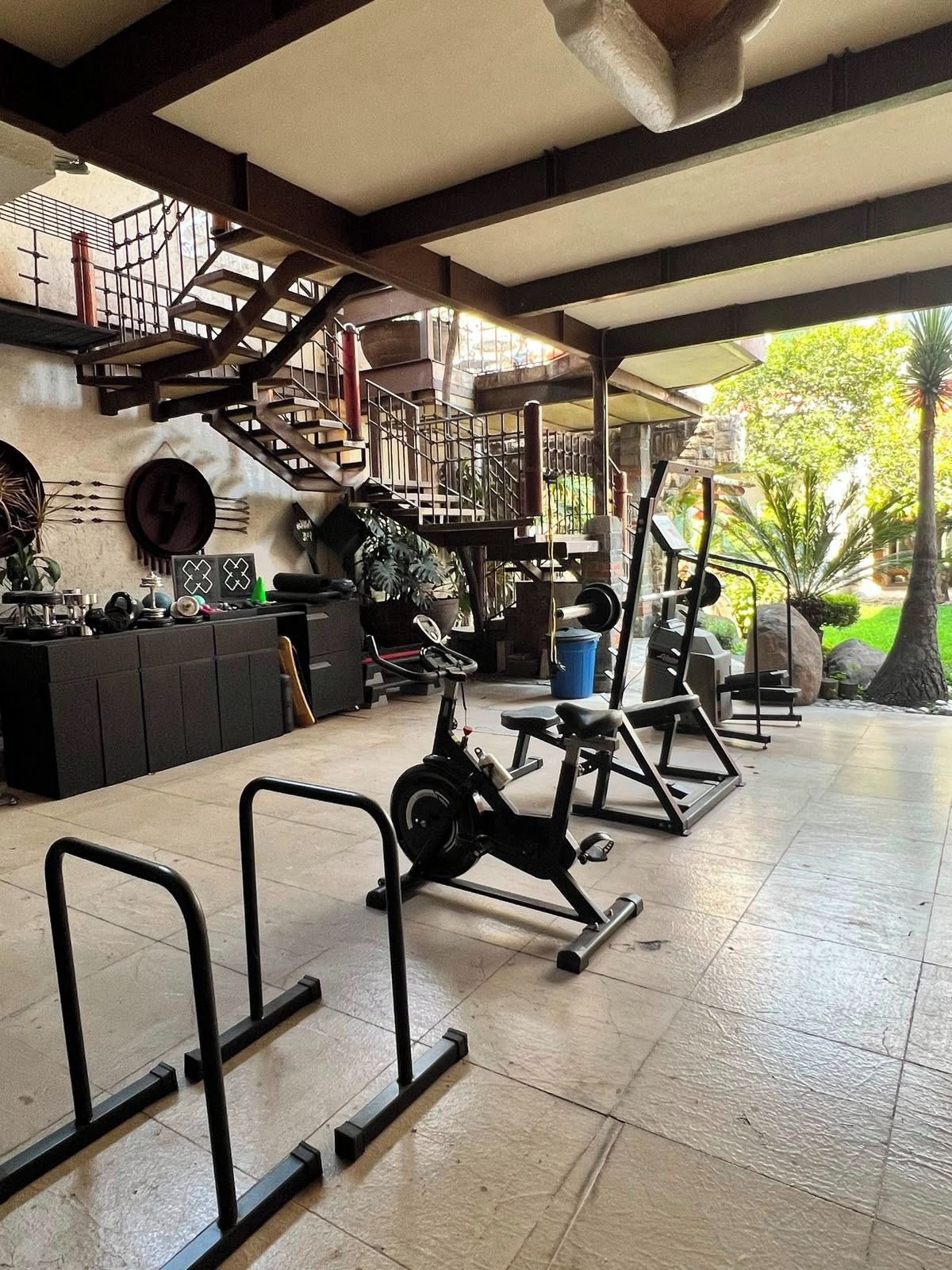 Un gimnasio con equipo de ejercicio, una escalera y vistas a zonas verdes.