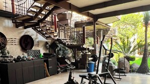 A gym with exercise equipment, a staircase, and a view of greenery outside. - Casa Sol (Mexico City)