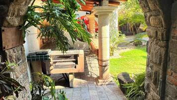 An outdoor stone archway leading to a patio area with a bench and a table, surrounded by greenery.