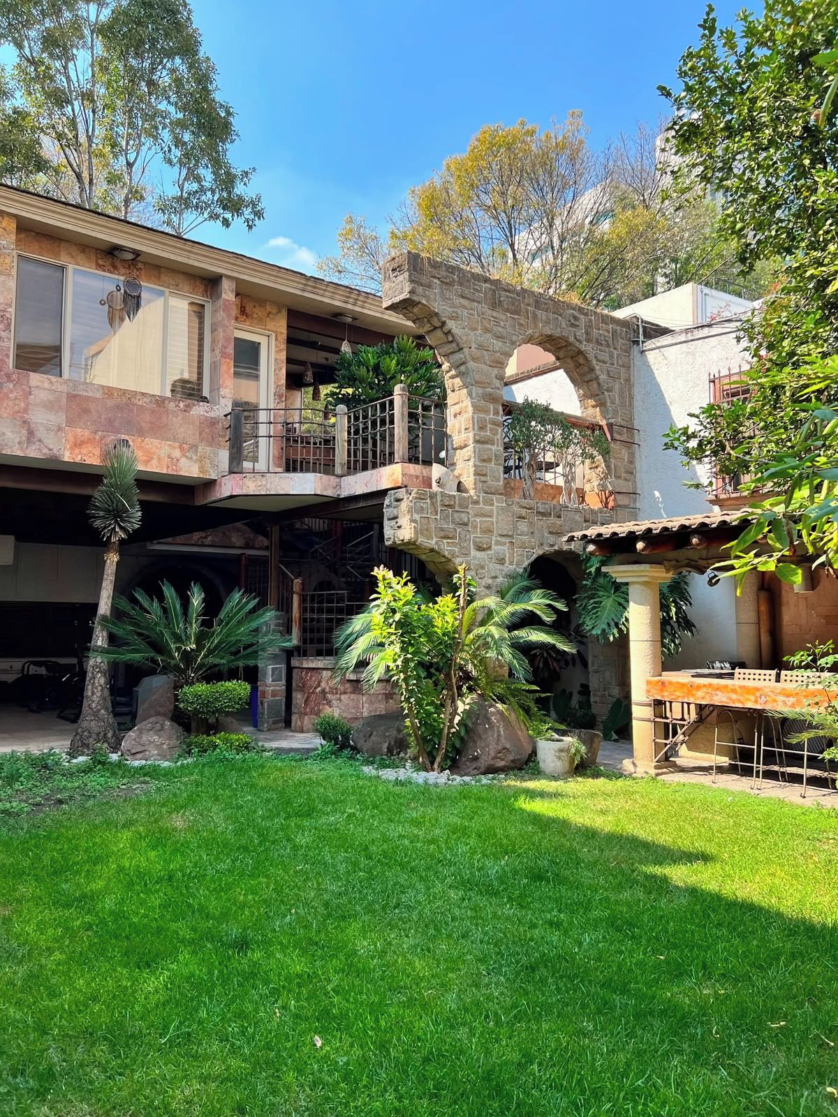 Una casa de dos pisos con un arco de piedra, un balcón y un césped bien cuidado.