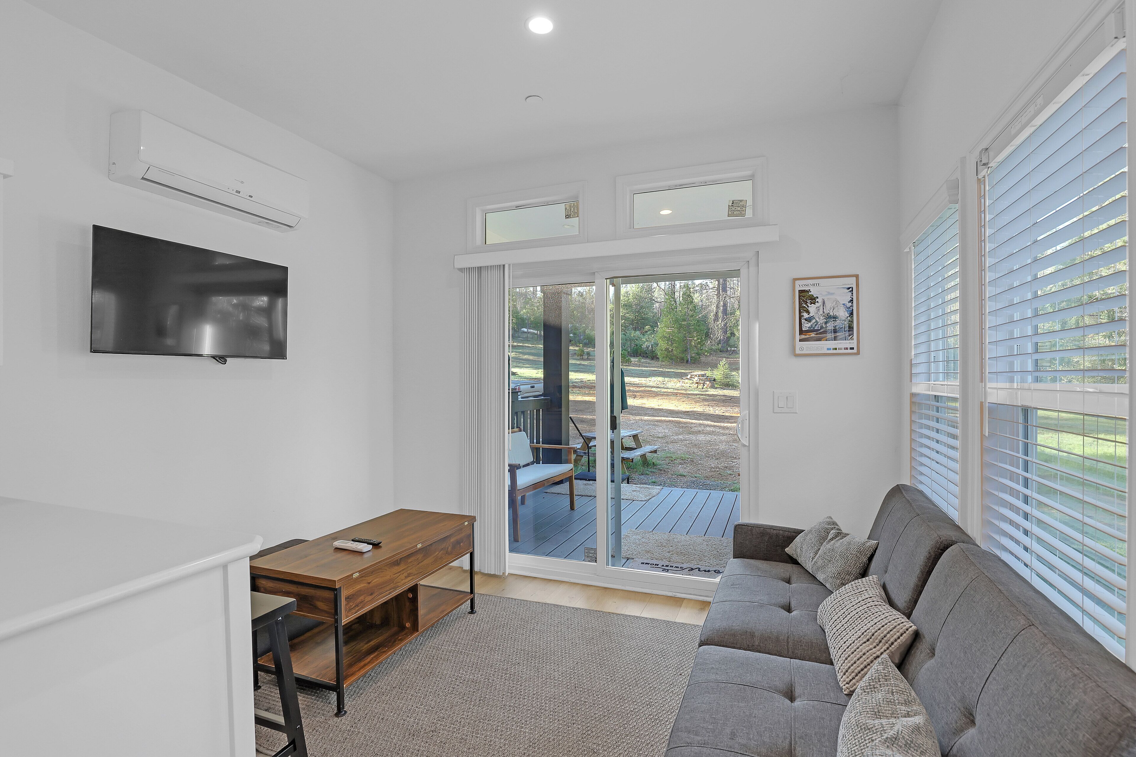 A living room with a sofa, a TV, a wooden table, and a sliding glass door leading to an outdoor area.