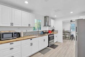A modern kitchen with white cabinetry, stainless steel appliances, a wooden countertop, and a dining area with a table and chairs. - Tiny House Village (Groveland)