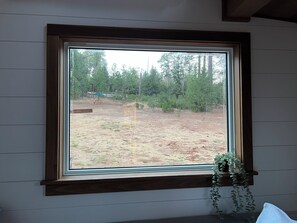 A room with a large window overlooking a yard with trees and a wooden bench.