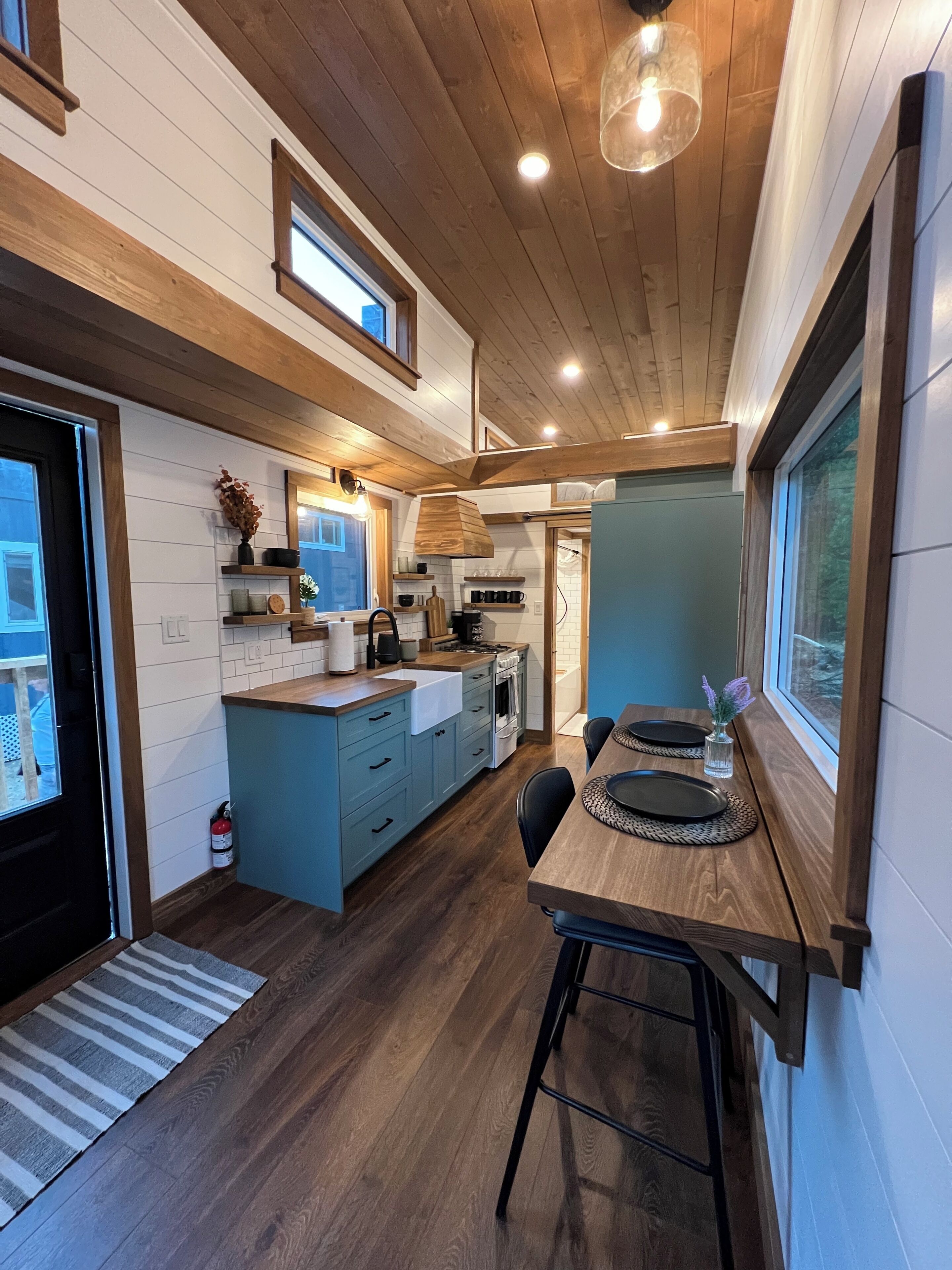 A modern kitchen with wooden cabinetry, a dining area with a wooden table, and a view through a window.