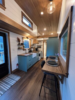 A modern kitchen with wooden cabinetry, a dining area with a wooden table, and a view through a window.