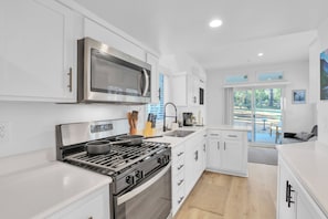 A modern kitchen with white cabinetry, stainless steel appliances, and a view of the outdoors through large windows.